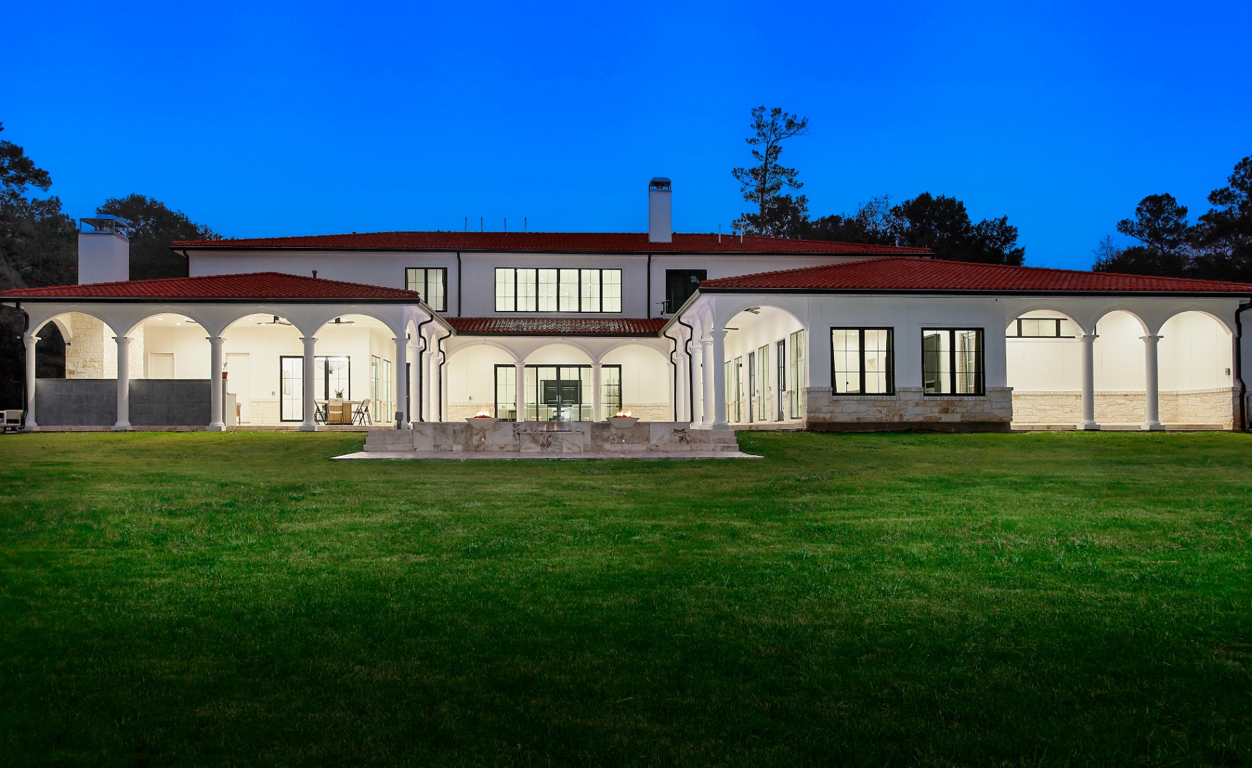 Rear elevation at twilight with sweeping loggia, fire features, and manicured lawn