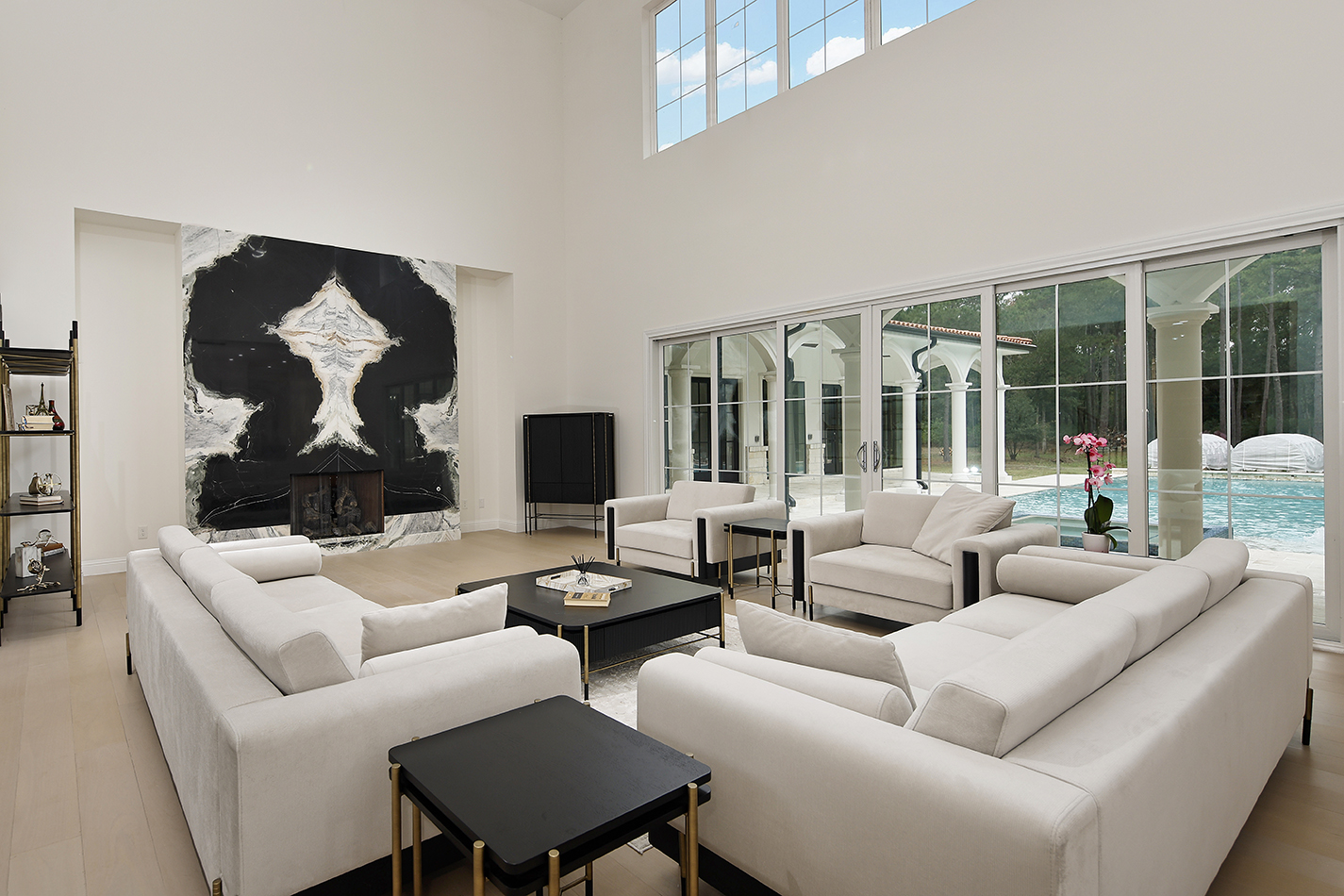 Great room with two-story ceilings, book-matched stone fireplace, and pool views